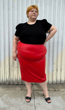 Load image into Gallery viewer, Full-body front view of a size 24 Eloquii bright red pleather midi pencil skirt styled with a black subtle puff sleeve tee and black kitten heels on a size 22/24 model. The photo is taken outside in natural lighting.
