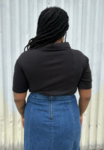 Load image into Gallery viewer, Back view of a size 16 Pretty Little Thing black collared bodysuit with bust cut-out styled tucked into a medium wash denim skirt on a size 14/16 model. The photo is taken outside in natural lighting.
