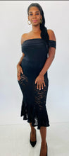 Load image into Gallery viewer, Full-body front view of this Fashion to Figure size 1 off-the-shoulder black bodysuit maxi dress with black lace overlay and mermaid-style skirt styled with black heels on a size 12 model.
