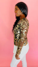 Load image into Gallery viewer, Side view of a size L Naeem Khan for 11 Honoré black long sleeve mesh semi-sheer blouse with intricate gold sequin pattern and details all throughout and sheer sleeves, styled with white trousers on a size 10/12 model.

