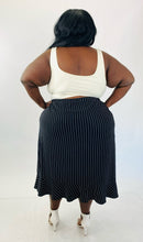 Load image into Gallery viewer, A full-body back view of a size 4X Maggie Barnes black maxi skirt with white pinstripes and a ruffle hem skirt styled with a white crop tank and white strappy heels on a size 24/26.
