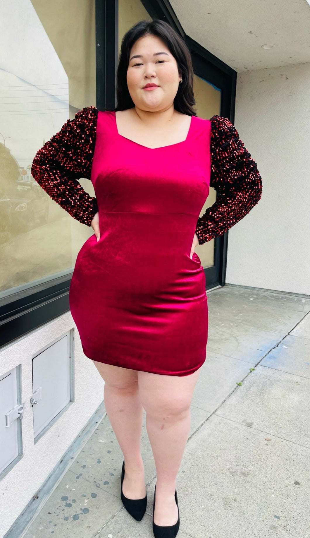 Full-body front view of a red velvet bodycon mini dress with black velvet puff sleeves with red sequins styled with black heels on a size 14/16 model.