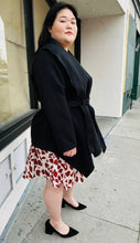 Load image into Gallery viewer, Full-body side view of a Bloomchic black collared coat with a handkerchief hem and a cinching belt styled over a cream and red dress on a size 14/16 model.
