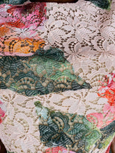 Load image into Gallery viewer, Close up detail shot of the white, pink, orange, and green colors in the embroidered lace overlay on this size 14 Monique Lhuillier for 11 Honoré white lace a-line mini dress with pink and green floral pattern, a high neck, and a voluminous skirt.
