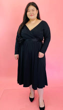 Load image into Gallery viewer, Full-body front view of a size 14 Runway Marc Jacobs x 11 Honoré black long sleeve empire waist midi dress with v-neck faux-wrap bodice and black belt with rosette detail styled with black pumps on a size 14/16 model.
