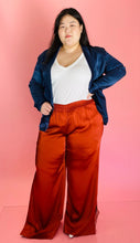 Load image into Gallery viewer, Full-body front view of a size 3 Baja East for 11 Honoré deep blue satin blazer with hook and eye closure and subtle puff sleeves styled with a white tee and rust orange silky pants on a size 14/16 model.
