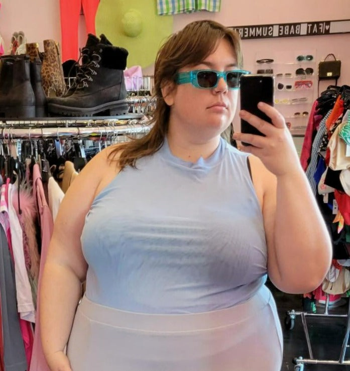 Close up view of a size 4XL WRAY bably blue mesh mockneck tank styled tucked into a pale blue mini skirt on a size 24 model.