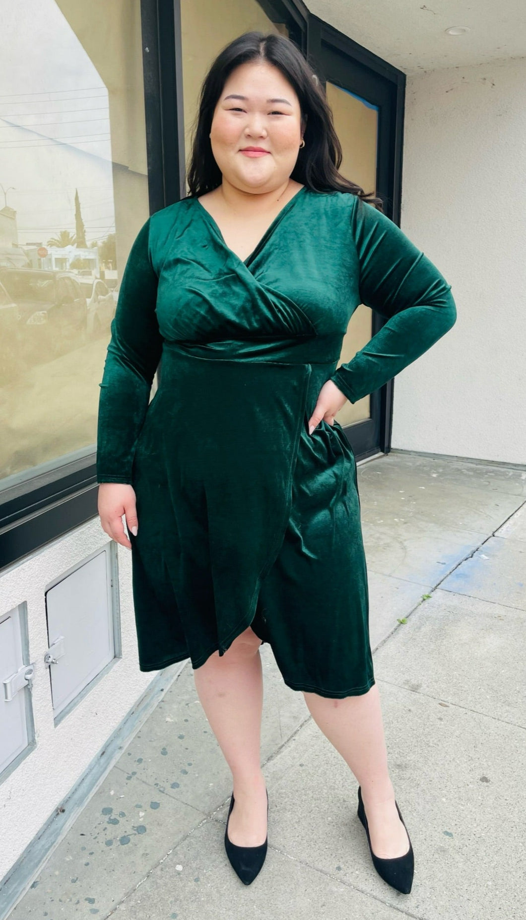 Full-body front view of a size 16 Bloomchic green velvet midi dress with tulip hem and long sleeves styled with black pumps on a size 14/16 model.