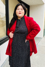 Load image into Gallery viewer, Front view of a size 14 Bloomchic deep red felt collared coat with belt styled open over a black and white polka dot maxi dress on a size 14/16 model.
