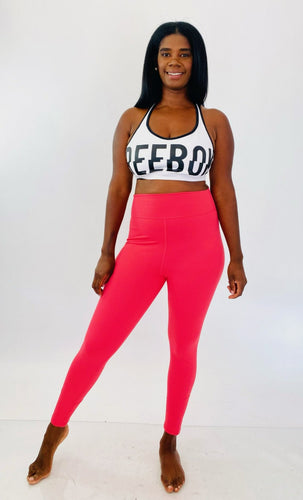 Full-body front view of a pair of size L fbf salmon pink active leggings styled with a white and black sports bra on a size 12 model.