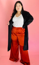 Load image into Gallery viewer, Full-body front view of a size 3 Baja East for 11 Honoré black satin duster trench with a belt styled open over a white tee and rust orange silky pants on a size 14/16 model.
