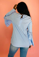 Load image into Gallery viewer, Back view of a size 12 Prabal Gurung for 11 Honoré light blue and white pinstriped blouse with high-neck knotted detail at the neckline, wide bell sleeves, and gold buttons styled with lightwash denim on a size 12 model.
