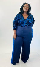 Load image into Gallery viewer, Full-body front view of these size 28 Eloquii navy blue wide leg trousers with light blue racing stripes down the sides styled with a navy blue crushed velvet bodysuit on a size 24/26 model.
