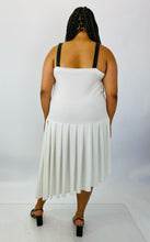 Load image into Gallery viewer, Full-body back view of a size 16 Jamie Wei Huang white asymmetrical hem midi dress with pleated skirt, pocket details, and faux leather straps styled with strappy black heels on a size 18/20 model.
