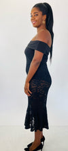 Load image into Gallery viewer, Full-body side view of this Fashion to Figure size 1 off-the-shoulder black bodysuit maxi dress with black lace overlay and mermaid-style skirt styled with black heels on a size 12 model.
