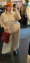 Load image into Gallery viewer, Additional full-body front view of a size 22 Eloquii off-white/cream all-over sequined button-up jumpsuit with tie belt styled with a maroon faux fur bag and black mary janes on a size 22/24 model.
