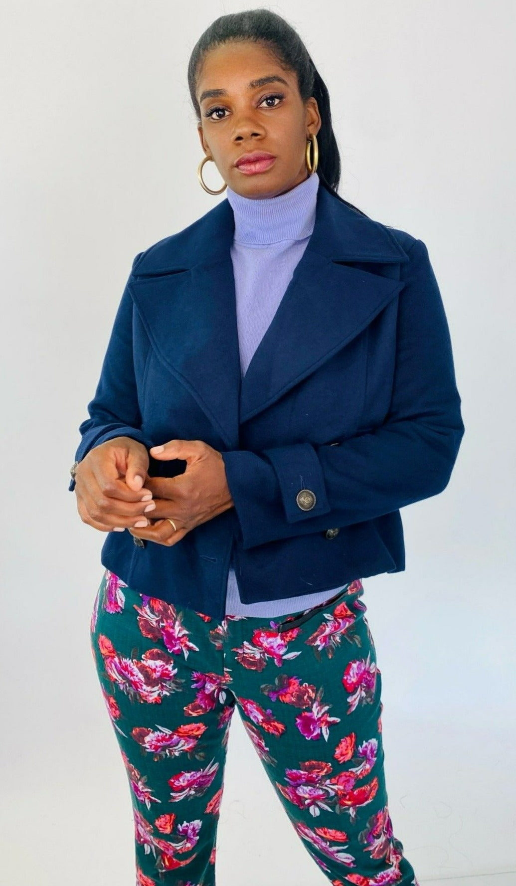 Front view of a size L BB Dakota navy blue blazer-style cropped peacoat styled with a periwinkle sweater and green floral pants on a size 12 model.