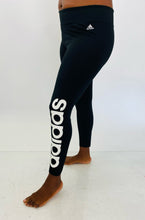 Load image into Gallery viewer, Half-side view of a pair of size XL Adidas black active leggings with the &quot;Adidas&quot; logo down the side on a size 12 model.
