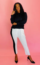 Load image into Gallery viewer, Full-body front view of a pair of size 3 Baja East for 11 Honoré crisp white drop-crotch tapered pants with a black side stripe and elastic waistband styled with a black blouse and black pumps on a size 12 model.
