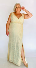 Load image into Gallery viewer, Full-body front view of a size 20 La Femme Curve shimmery champagne yellow gown with a faux wrap bust and high side slit, highlighting the slit detail and styled with tan pumps on a size 18/20 model.
