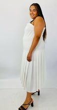 Load image into Gallery viewer, Full-body side view of a size 16 Jamie Wei Huang white asymmetrical hem midi dress with pleated skirt, pocket details, and faux leather straps styled with strappy black heels on a size 18/20 model.
