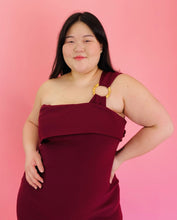 Load image into Gallery viewer, Closer view of the bodice, fold-over neckline, and one-shoulder circle ring strap detail on a size 18 Haney for 11 Honoré burgundy one-shoulder bodycon midi dress with a fold-over bust detail, circle ring strap detail, and slit at the front on a size 14/16 model.

