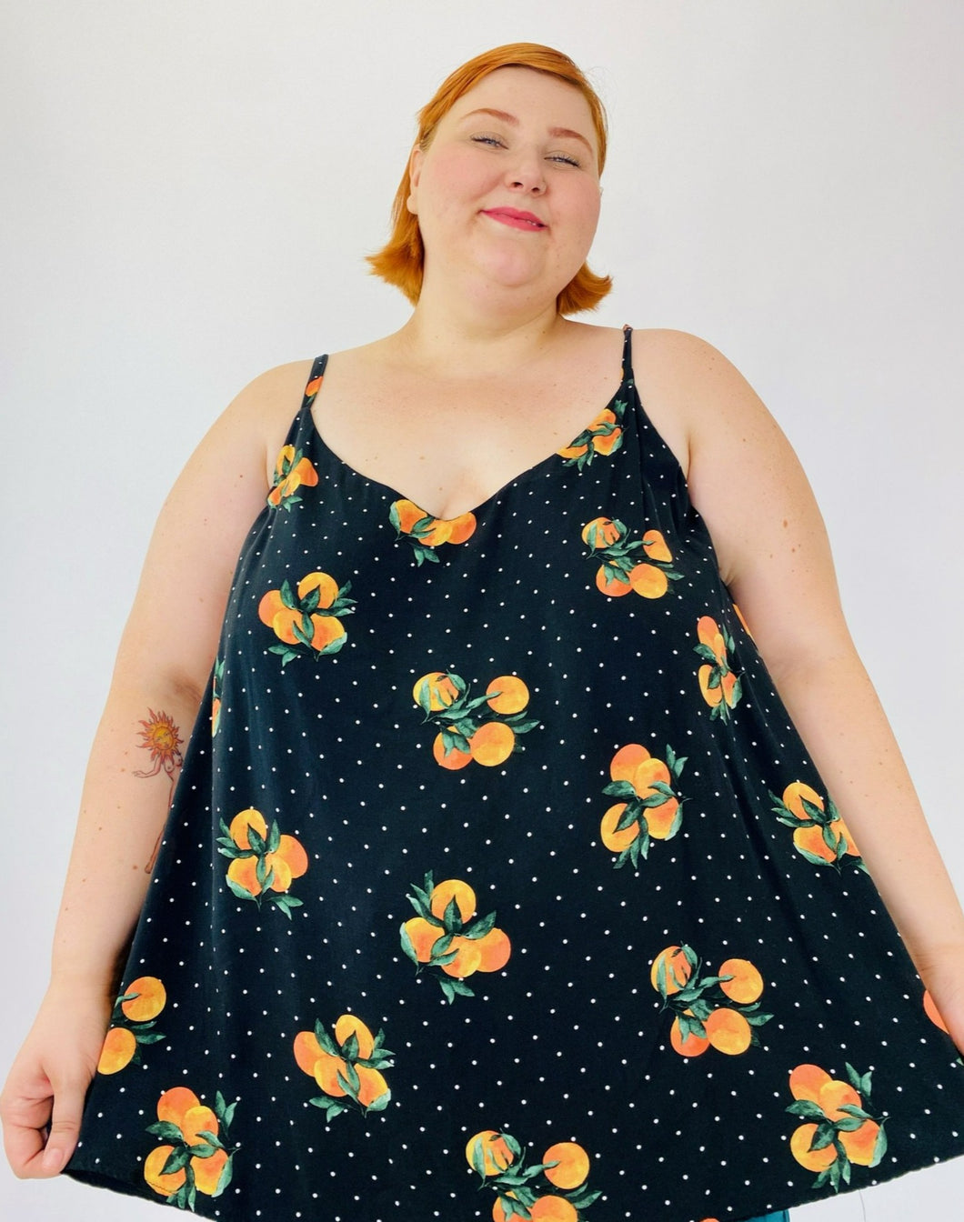 A size 4 Torrid black flowy tank top with an orange pattern and white mini polka dots on a size 22 model. The straps are adjustable.