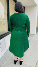 Load image into Gallery viewer, Full-body back view of a size 14 Bloomchic emerald green shimmer over black tulip hem midi dress with long sleeves, a cross-detail bust, and a subtle high-low styled with black heels on a size 14/16 model.
