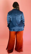 Load image into Gallery viewer, Full-body back view of a size 3 Baja East for 11 Honoré deep blue satin blazer with hook and eye closure and subtle puff sleeves styled with a white tee and rust orange silky pants on a size 14/16 model.
