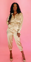 Load image into Gallery viewer, Full-body front view of a size 12 Haney for 11 Honoré gold, sand color collared button-up jumpsuit with belt and tapered, crop ankle detail styled with tan pumps on a size 12 model. 
