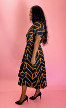 Load image into Gallery viewer, Full-body side view of a size 14 Maria Cornejo for 11 Honoré black and rust orange chevron patterned v-neck a-line maxi dress styled with black pumps on a size 12 model.
