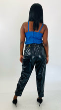 Load image into Gallery viewer, Full-body back view of these sexy size 14 Tanya Taylor black pleather high waisted tapered trousers with belt and gold hardware styled with a blue pleather tank and black pumps on a size 12 model.
