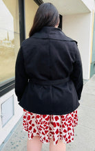 Load image into Gallery viewer, Back view of a Bloomchic black collared coat with a handkerchief hem and a cinching belt styled over a cream and red dress on a size 14/16 model.
