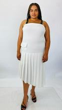 Load image into Gallery viewer, Full-body front view of a size 16 Jamie Wei Huang white asymmetrical hem midi dress with pleated skirt, pocket details, and faux leather straps styled with strappy black heels on a size 18/20 model.
