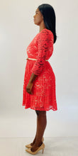 Load image into Gallery viewer, Full-body side view of a size 16 Eliza J coral lace long sleeve pleated midi dress with cream lining underneath and cream skinny belt styled with tan patent leather heels on a size 12 model.
