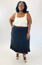 Load image into Gallery viewer, A full-body front view of a size 4X Maggie Barnes black maxi skirt with white pinstripes and a ruffle hem skirt styled with a white crop tank and white strappy heels on a size 24/26.
