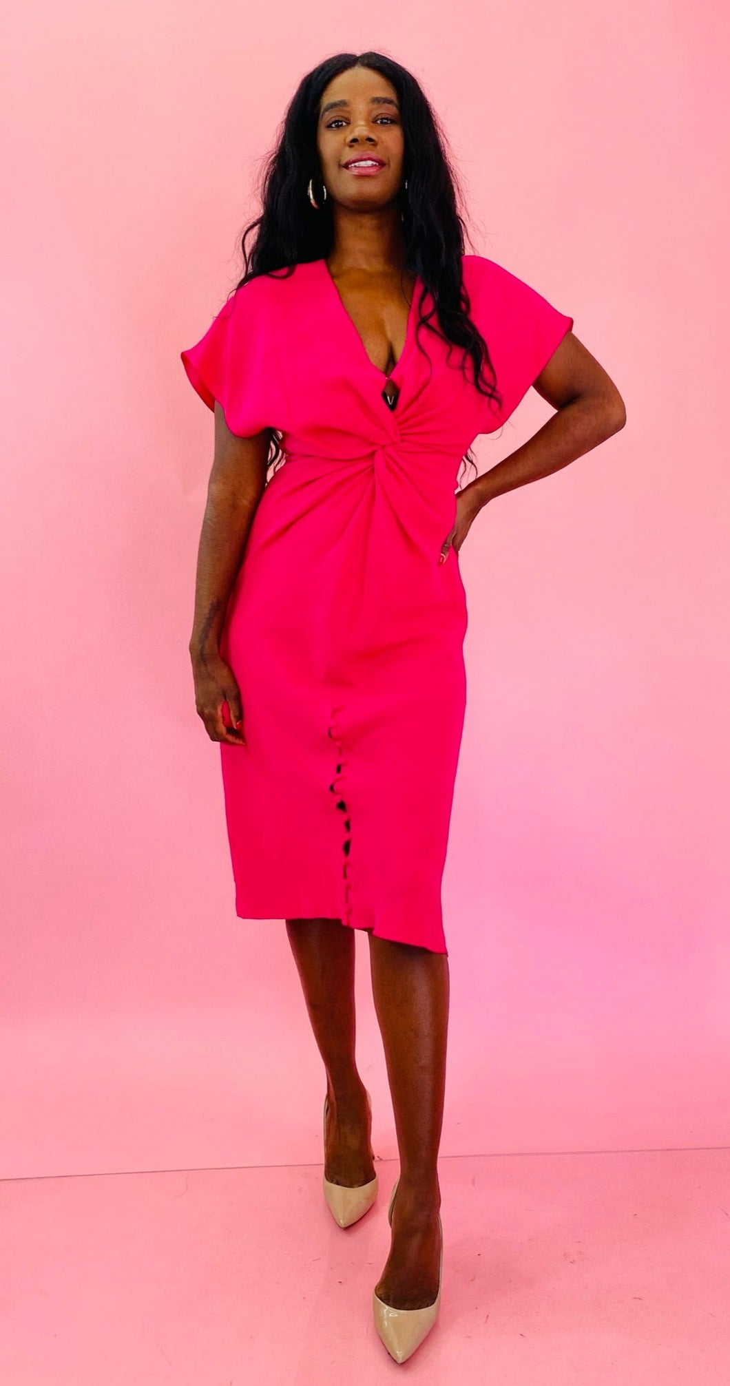 Full-body front view of a size 12 hot pink sheath dress with knotted torso detail, flutter sleeves, and fabric buttons at the hem styled with tan pumps on a size 10/12 model.
