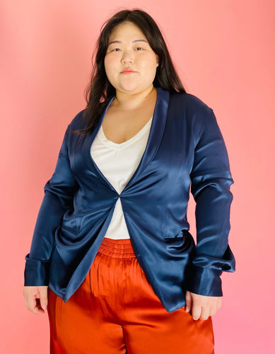 Front view of a size 3 Baja East for 11 Honoré deep blue satin blazer with hook and eye closure and subtle puff sleeves styled with a white tee and rust orange silky pants on a size 14/16 model.