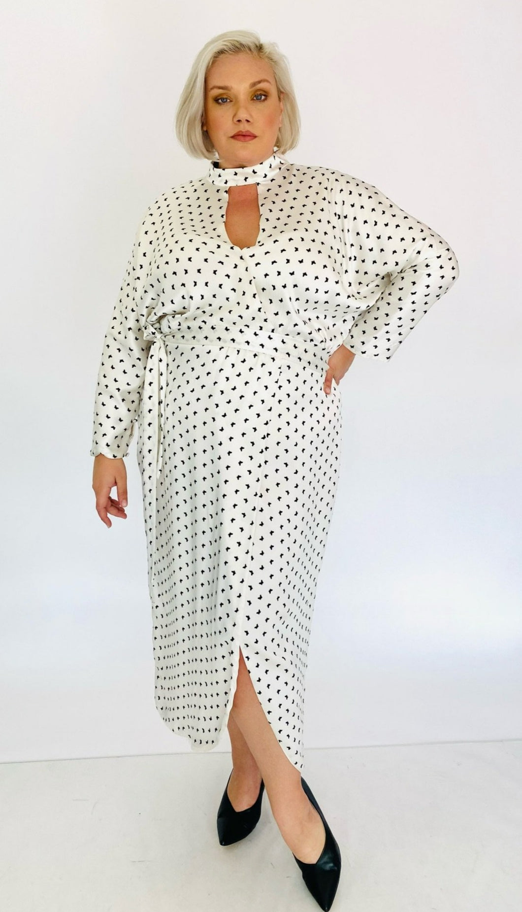 Full-body front view of a Monique Lhuillier for 11Honoré silky white gown with black mini butterfly print, choker and kethole details, and puff sleeves styled with black pumps on a size 18/20 model.
