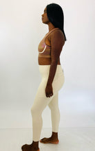 Load image into Gallery viewer, Full-body side view of a size L Fabletics brown high-neck active crop top with rainbow metallic shift styled with cream colored leggings on a size 12 model.
