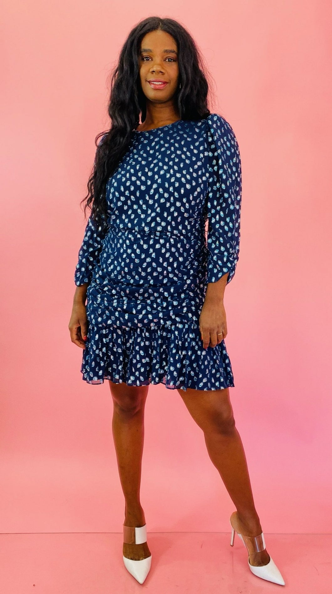 Full-body front view of a size 14 Tanya Taylor for 11HONORÉ navy blue long sleeve mini dress with light blue, and metallic silver swiss dot sheer overlay, ruffles and gathering, and a high neck styled with white heels on a size 10/12 model.