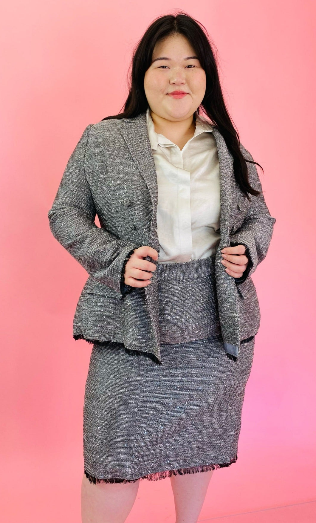 Front view showing off the fit at the torse of a size 18 Lela Rose gray tweed, textured blazer and skirt 2-piece suit set with black unfinished fringe hem styled with an off-white button-up top on a size 14/16 model.