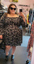 Load image into Gallery viewer, Full-body front view of a size 26 ASOS black mini dress with white, blue, and pink mini floral pattern all throughout styled with black sunnies and black mules on a size 22/24 model.
