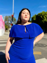 Load image into Gallery viewer, An outside shot of a size 14/16 model wearing a size 16 Reem Acra for 11 Honoré cobalt blue midi dress with capelet detail, keyhole bust, and handkerchief hem. The sunlight really highlights how vibrant the cobalt blue of this piece is!

