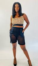 Load image into Gallery viewer, Full-body front view of a size XXL Adam Selman yellow and brown leopard print sports bra styled with black mesh shorts and black pumps on a size 12 model.
