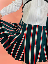 Load image into Gallery viewer, Close up detail shot of the green skirt and the buttons on this a size L TOME for 11 Honoré white, blue, red, and black mixed pinstripe and triple stripe collared button-up shirt dress with tie belt on a size 14/16 model.
