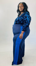 Load image into Gallery viewer, Full-body side view of these size 28 Eloquii navy blue wide leg trousers with light blue racing stripes down the sides styled with a navy blue crushed velvet bodysuit on a size 24/26 model.
