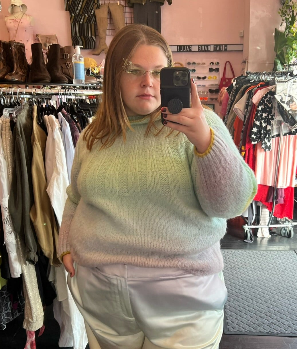 Front view of a size 2X Anthropologie pastel green, blue, and purple ombre mockneck sweater styled with pastel rainbow pants on a size 22/24 model.
