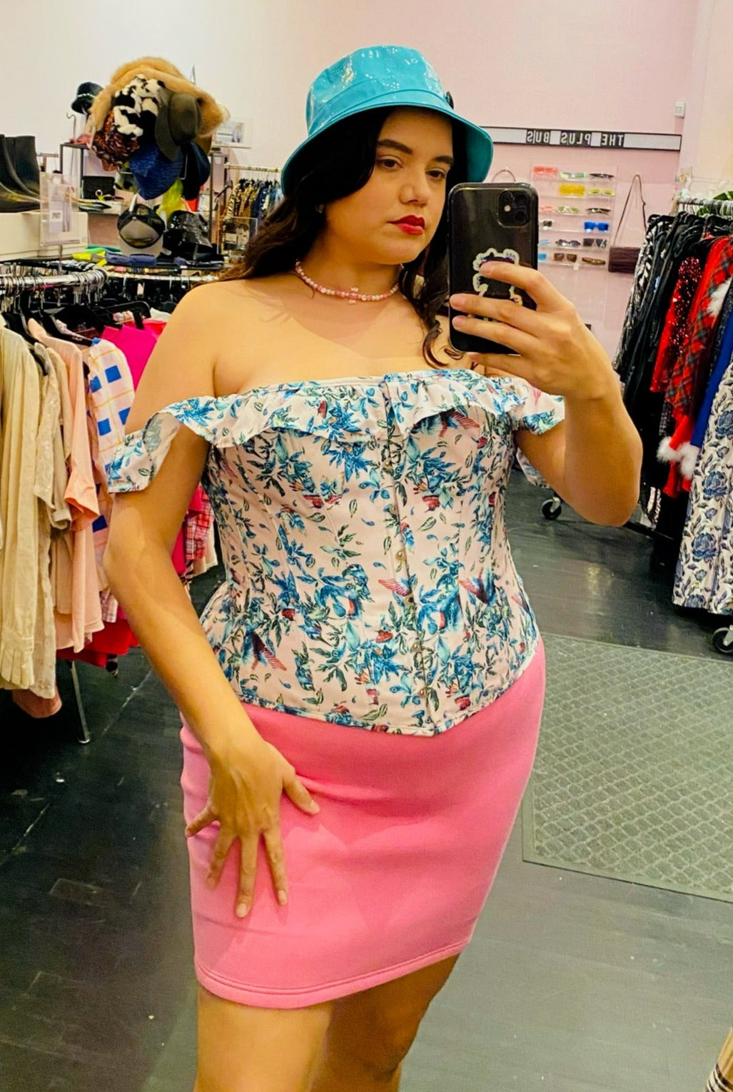 Front view of a size XL Lezé the Label stretchy bubblegum pink mini skirt styled with a blue and pink corset top and a blue bucket hat on a size 14/16 model.