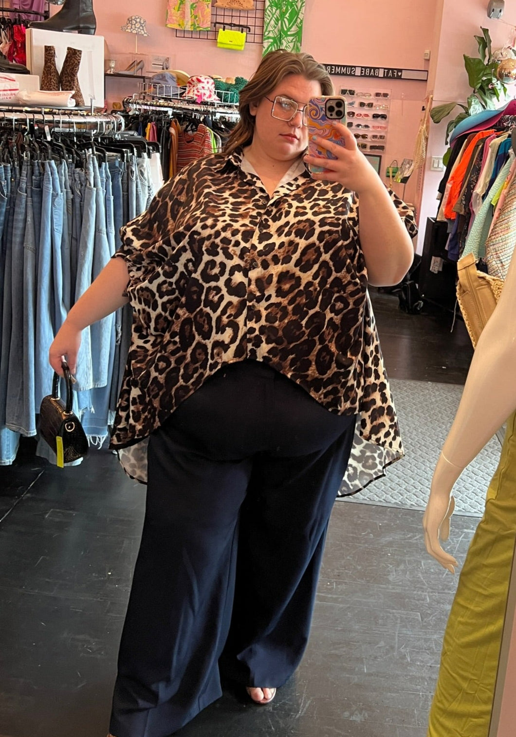 Full-body front view showing off a size 3/4X Thick brown and black leopard print button-up high-low blouse styled with navy blue trousers on a size 24 model.